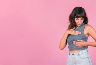 Mujer revisándose los senos con informe médico de cáncer de mama