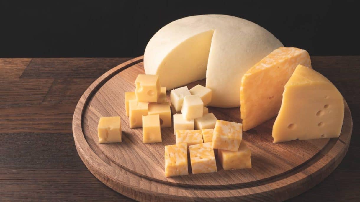 Variedad de quesos grasos como cheddar y brie sobre una tabla de madera.
