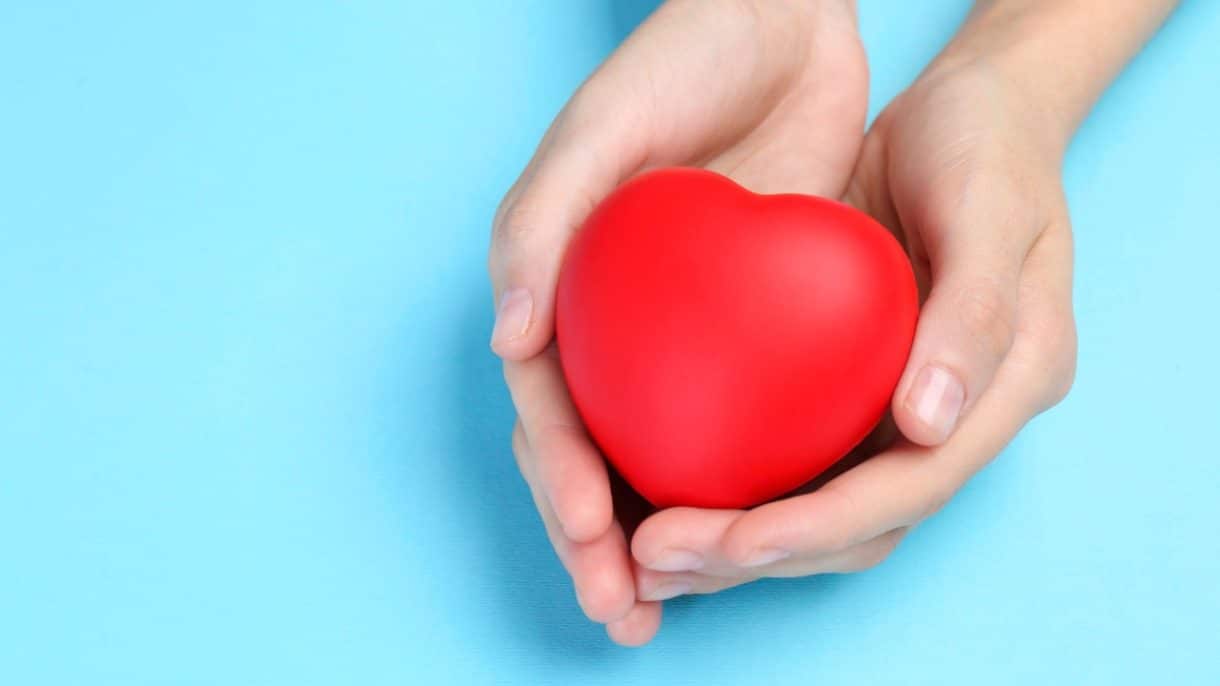 Representación visual de un corazón protegido por manos humanas sobre un fondo suave.